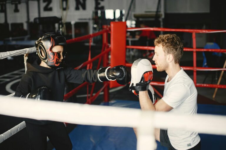 A child trainee learning boxing techniques with a coach inside a gym setup.