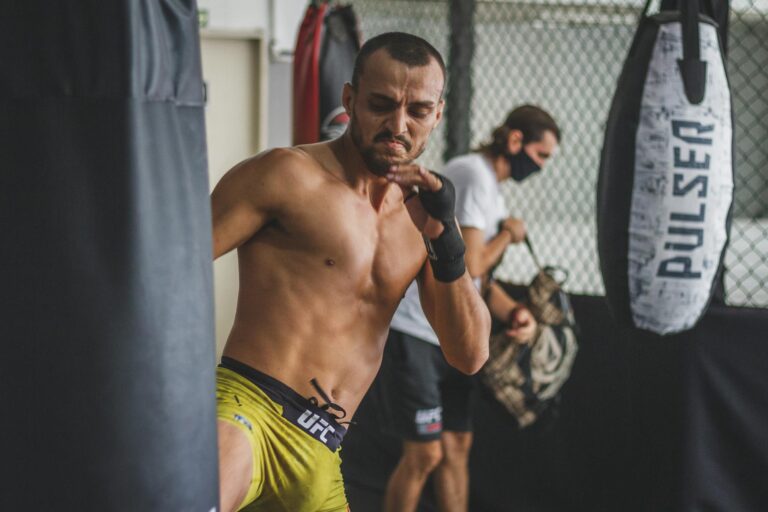 A determined man fiercely trains with a heavy bag inside a gym setting, showcasing athletic focus and strength.