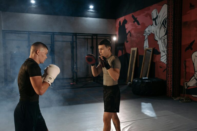 Two men engaged in an intense MMA training session indoors with boxing gear.